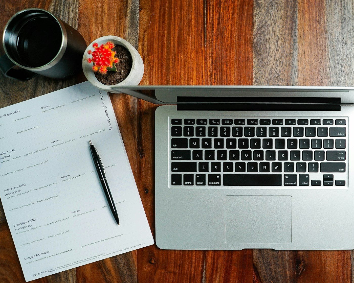 A laptop, notepad and pen laid out on a wooden desk