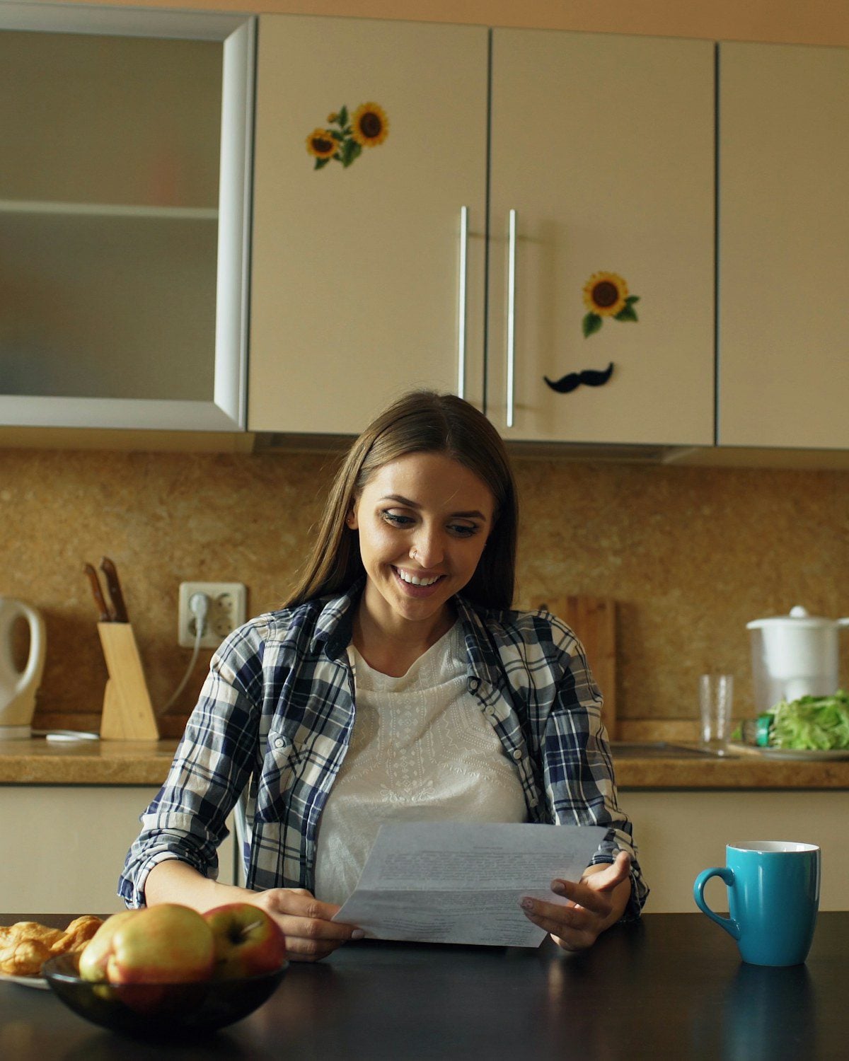 A woman sitting at a kitchen table reading a document, with a cup of tea beside her